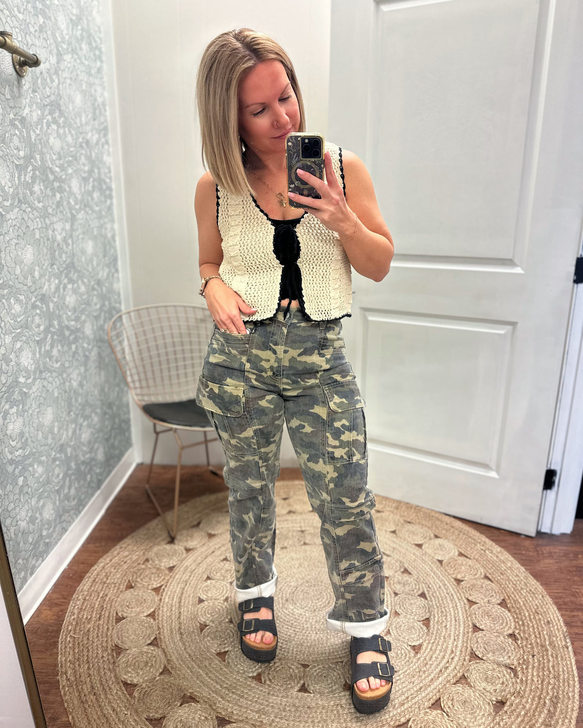 Cream crochet vest trimmed with black woven ribbon that front ties into bows. Paired with camo cargo pants and black sandals.