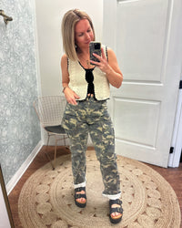 Cream crochet vest trimmed with black woven ribbon that front ties into bows. Paired with camo cargo pants and black sandals.