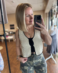 Cream crochet vest trimmed with black woven ribbon that front ties into bows.