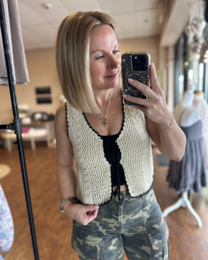 Cream crochet vest trimmed with black woven ribbon that front ties into bows.